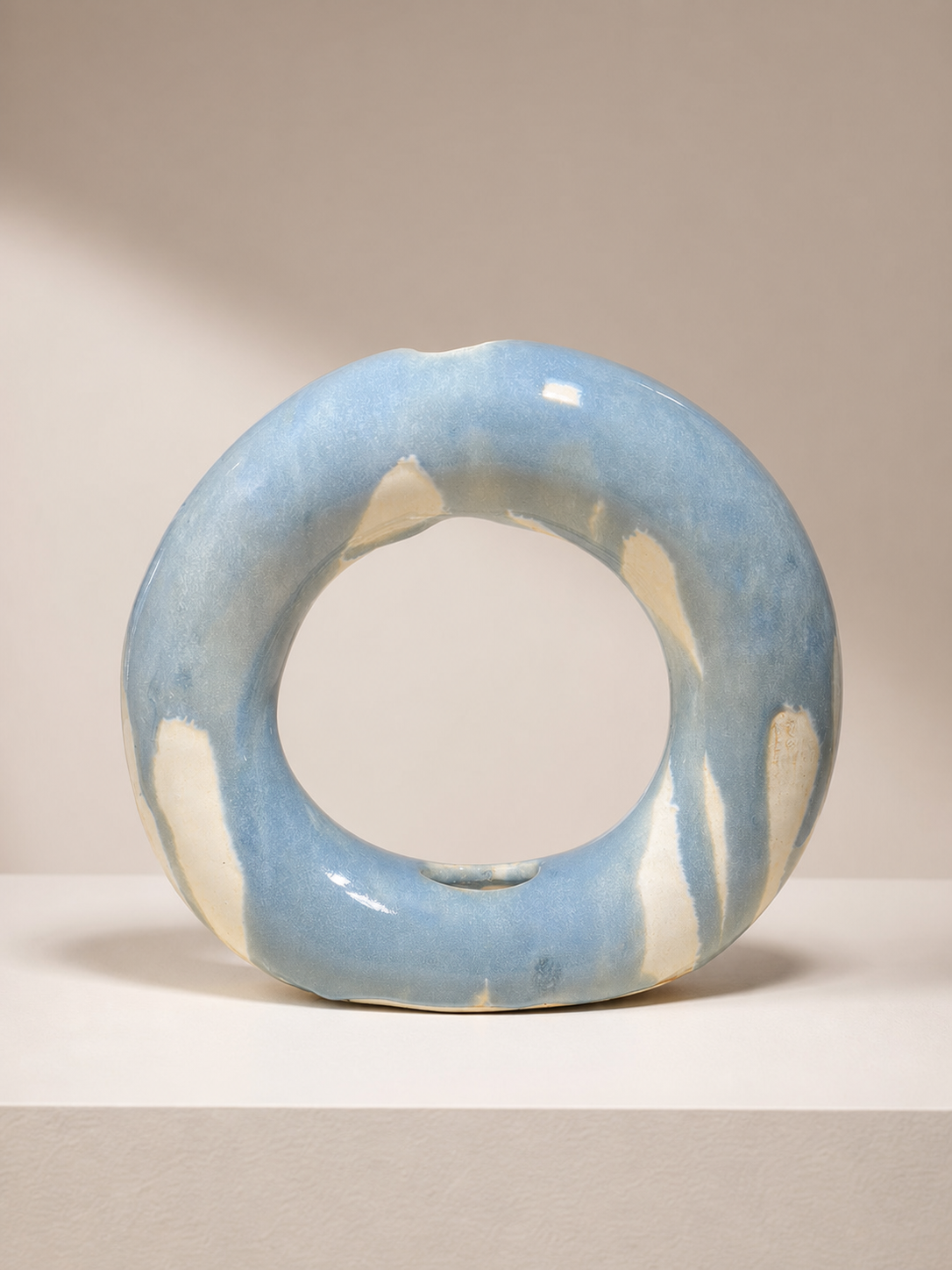 A light blue ceramic donut vase with dripped glaze.